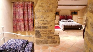 Ein Schlafzimmer mit Steinwand, einem Bett mit gemusterten Betttextilien und einem Fenster mit Vorhängen.