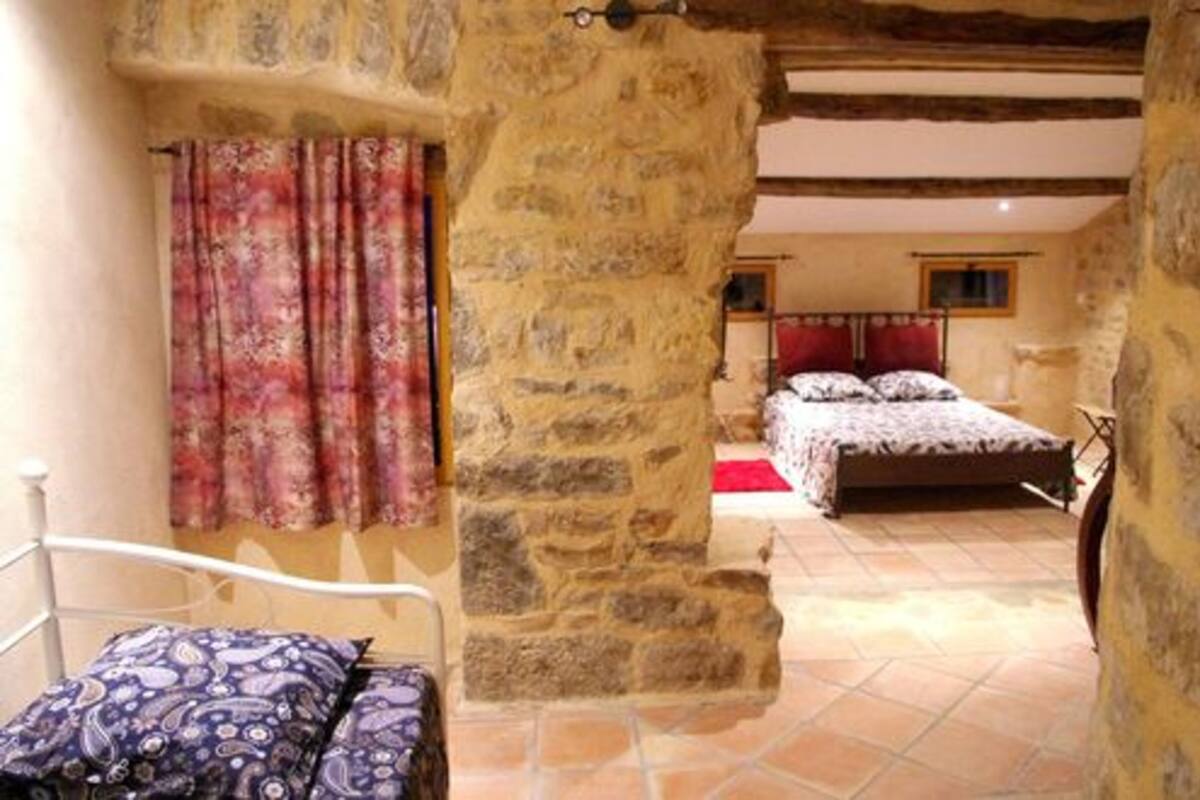 Un dormitorio con pared de piedra, cama con ropa de cama estampada y ventana con cortinas.
