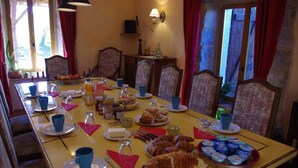 Ein Esstisch, reichhaltig gedeckt mit Speisen und Getränken, umgeben von stuhligen Sitzgelegenheiten mit Muster.