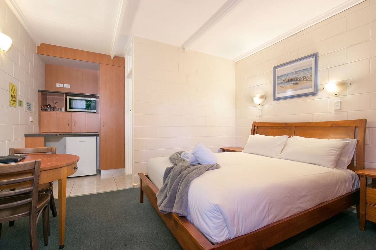 A bedroom with a wooden bed, a small desk, and a kitchenette.