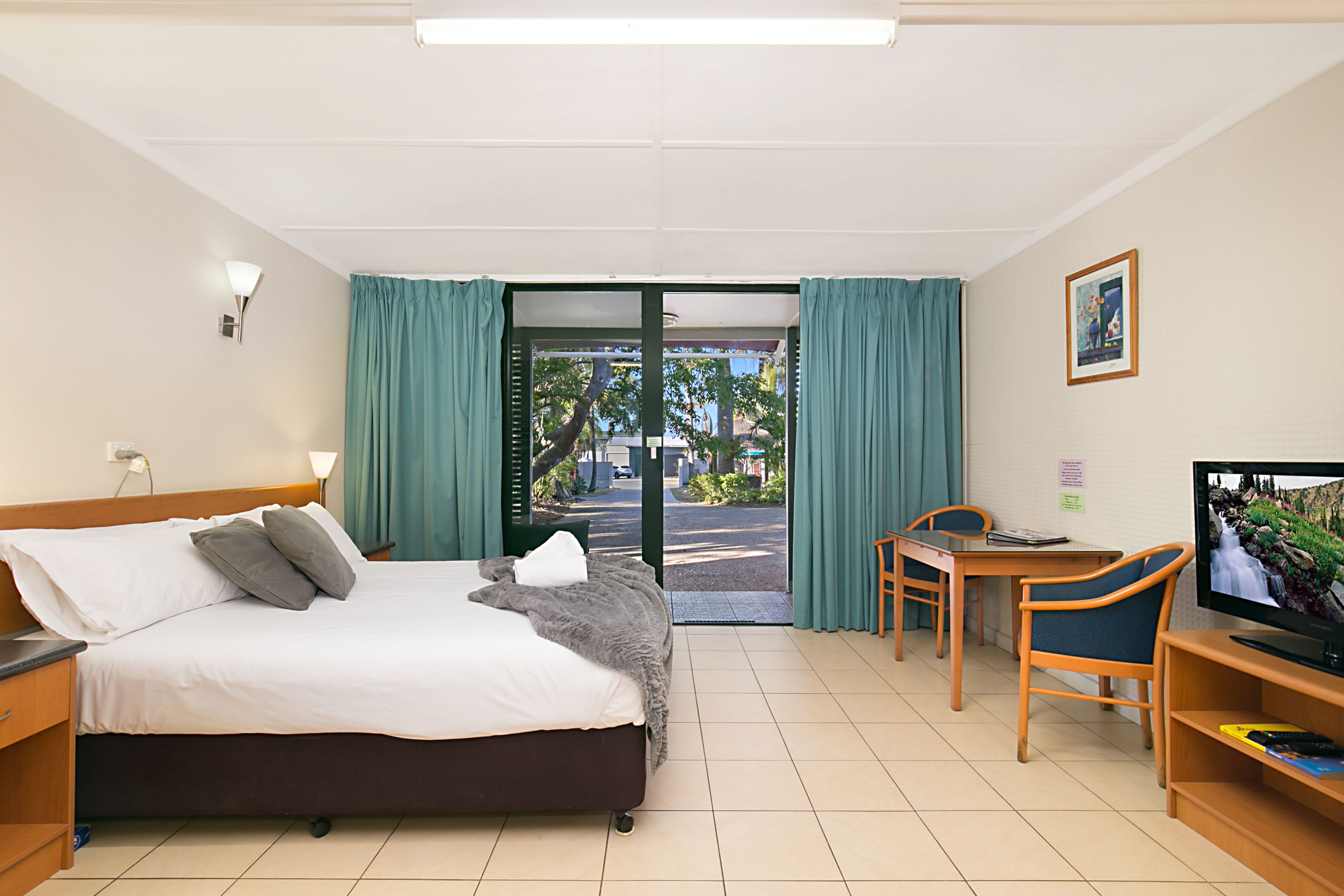 A hotel room with a bed, a desk, a chair, a television, and a view of the outside.