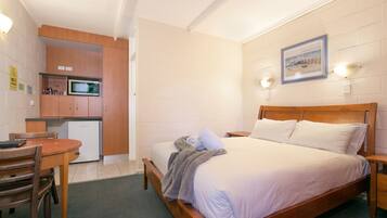 A bedroom with a wooden bed, a small desk, and a kitchenette.