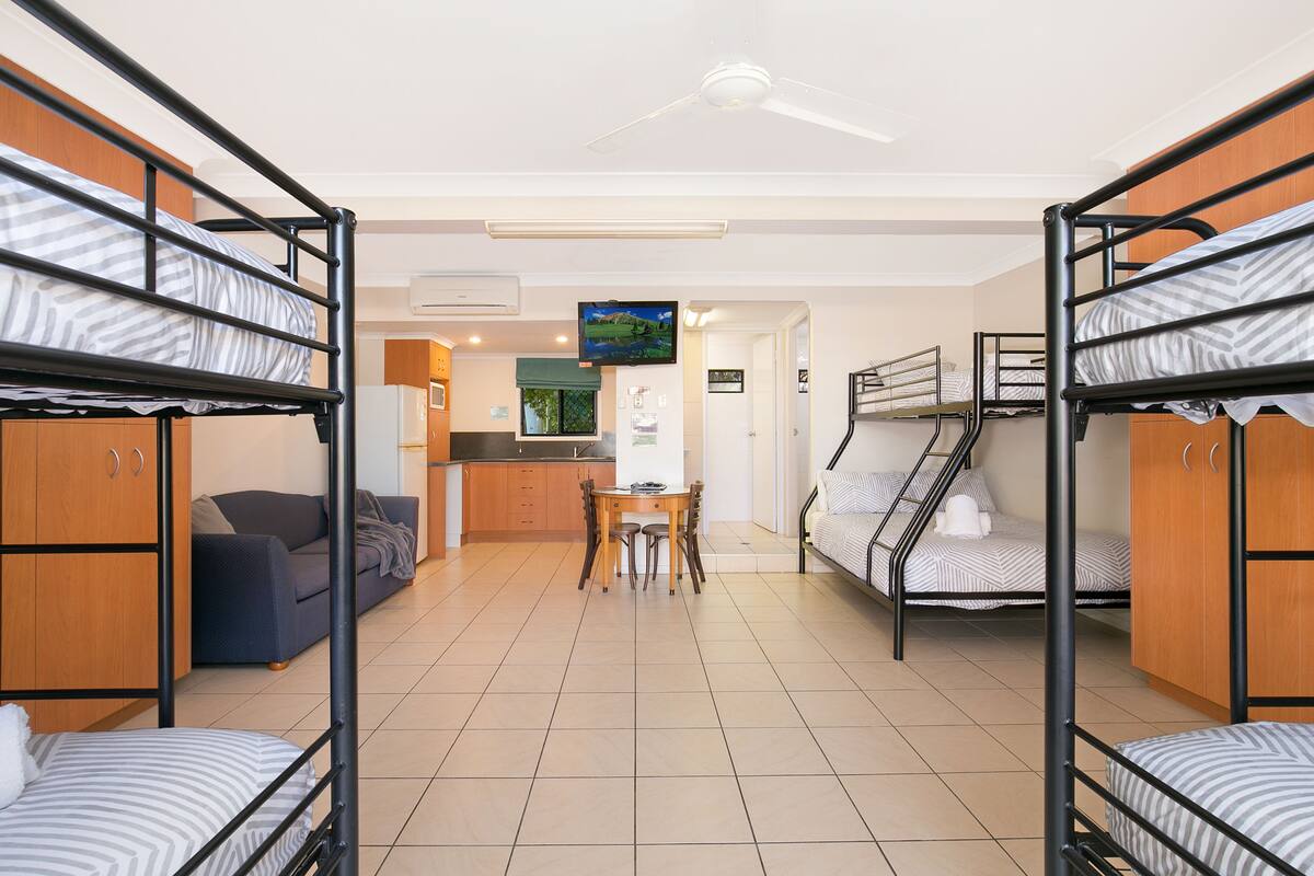 A dormitory room with bunk beds, a kitchenette, a dining area, and a TV.