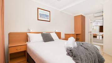 A hotel room with a bed, a nightstand, a wooden wardrobe, a bathroom with a sink and mirror.