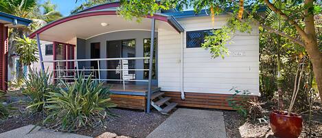 A single-story mobile home with a covered porch, a small deck, and a potted plant.