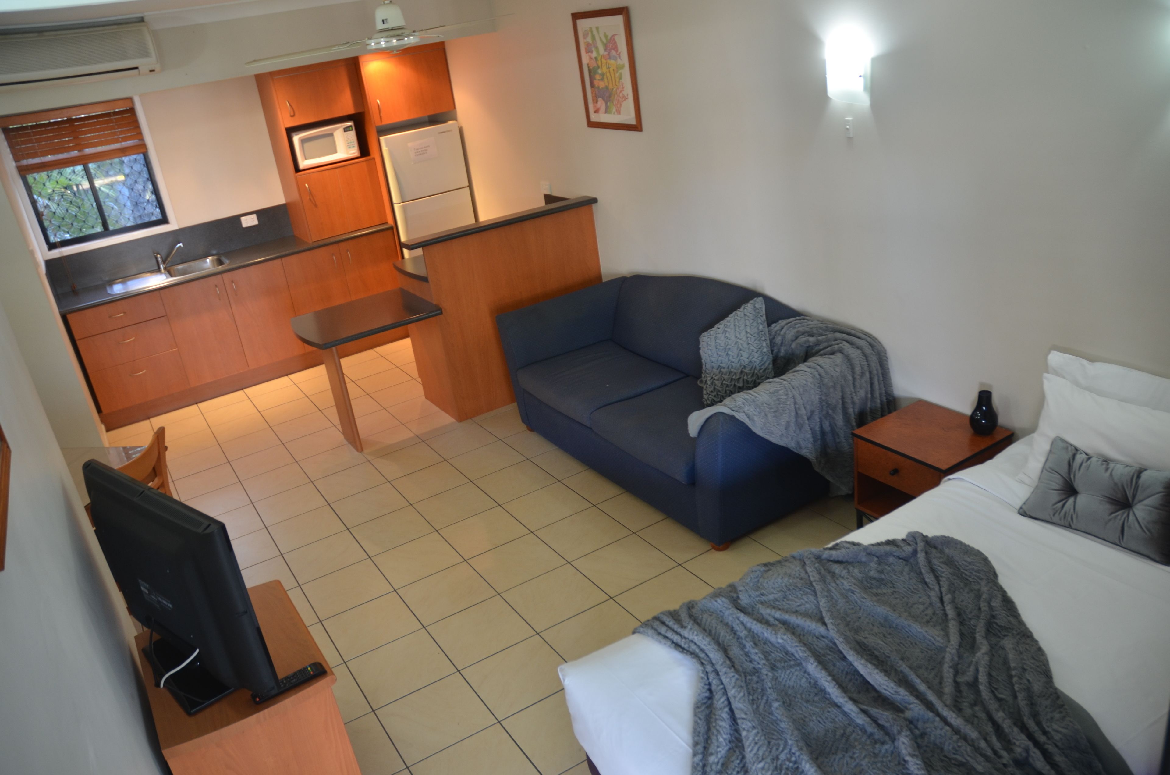 A compact hotel room with a kitchenette, a sofa, a bed, and a TV.