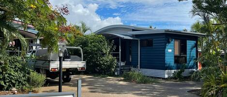 A mobile home with a blue exterior, a gravel driveway, and surrounding greenery.