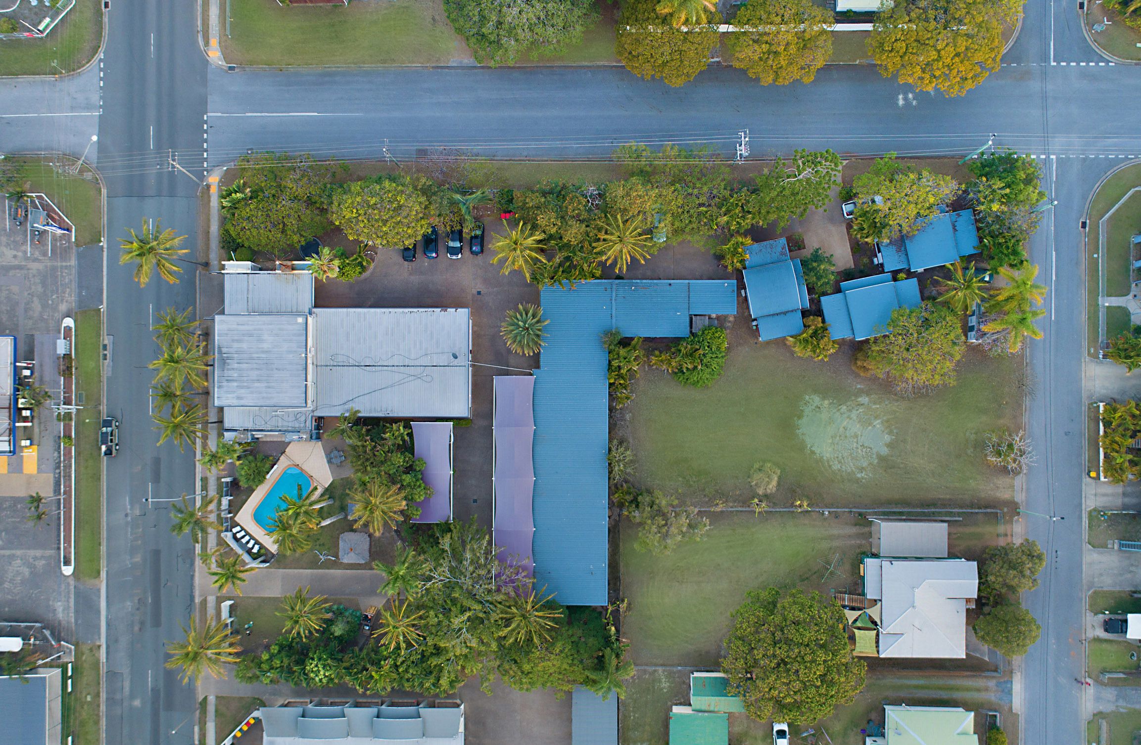 An aerial view of a residential area with a blue-roofed house, a swimming pool, and several palm trees.
