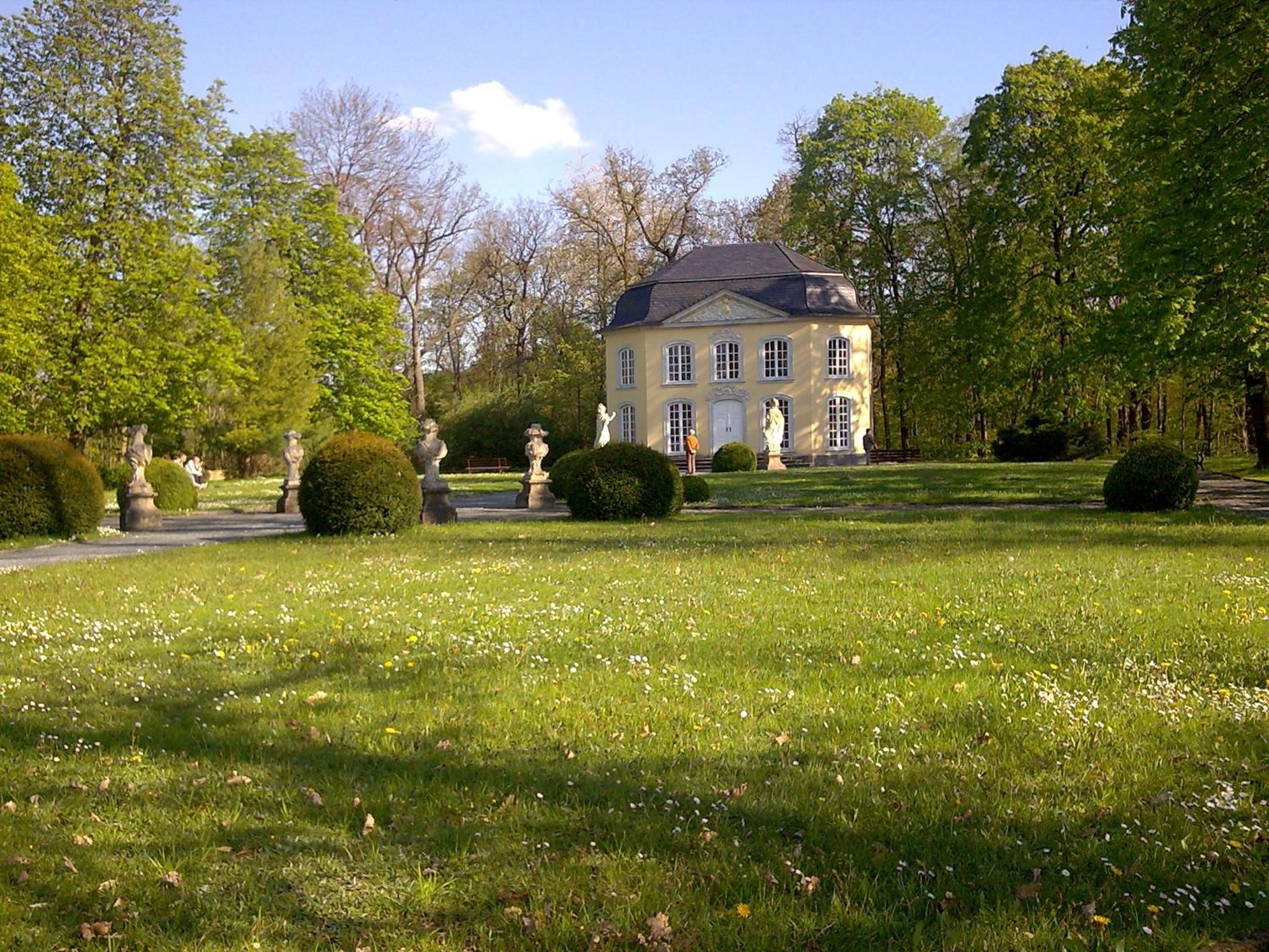 A large, classical-style building with a symmetrical facade, surrounded by manicured lawns and a variety of statues.