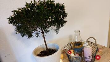Un arbre en pot orné de fleurs blanches, une bouteille en verre et un panier contenant des bougies et des décorations, le tout posé sur une étagère en bois.