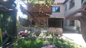 A house with a wooden deck, a stone wall, and colorful string lights. - Ferienwohnung Brunow (Neundorf)