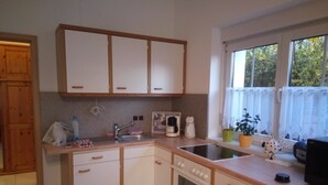 A kitchen with white cabinets, a sink, a stove, and a window with a view of trees. - Ferienwohnung Brunow (Neundorf)