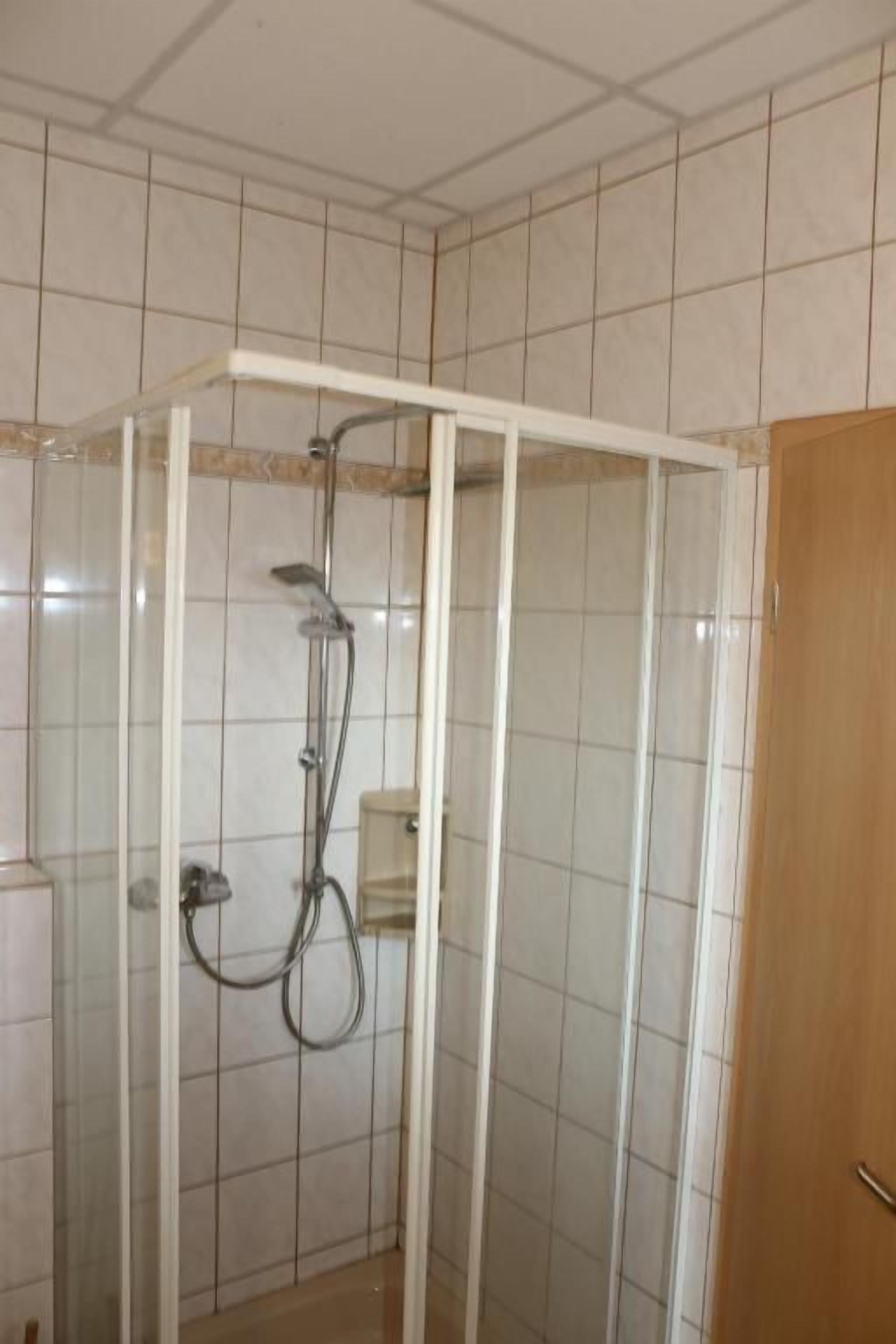 Lasiseinällä varustettu suihkukaappi, jossa on myös suihkupää ja ohjauspaneeli.