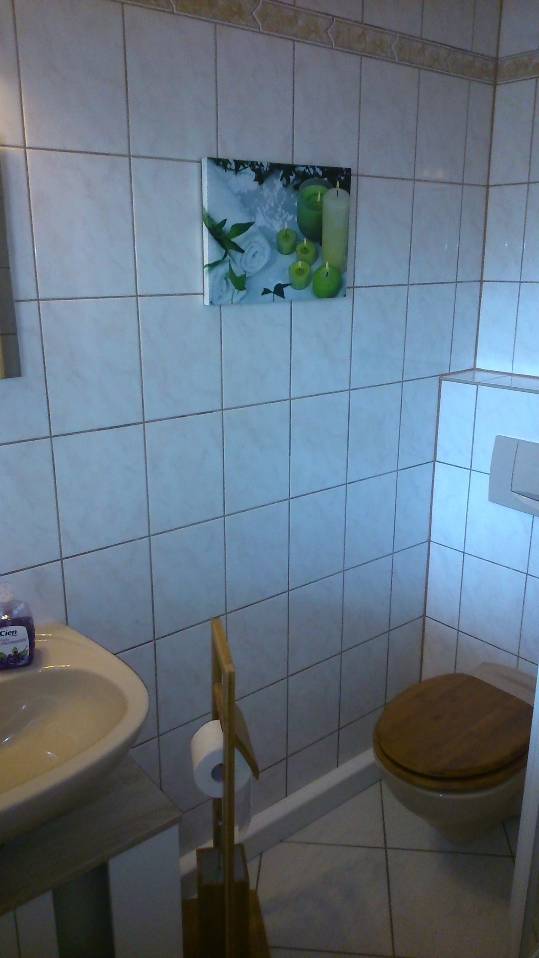 A bathroom with a toilet, sink, and a wall-mounted picture of green apples and white flowers.