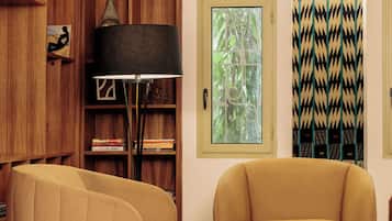 Una habitación con sofá, una mesita, lámpara, estantería y ventana con vistas a árboles.