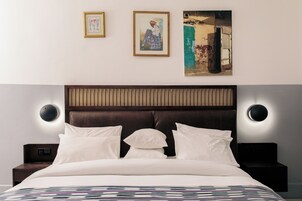 Una habitación de hotel con una cama, dos cuadros en la pared y una mesita de noche con una lámpara.