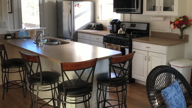 Una cocina moderna con armarios blancos, electrodomésticos de acero inoxidable, una isla grande con taburetes de bar y un comedor.