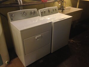 A front view of a laundry room with two stacked front-loading washing machines and a single sink.