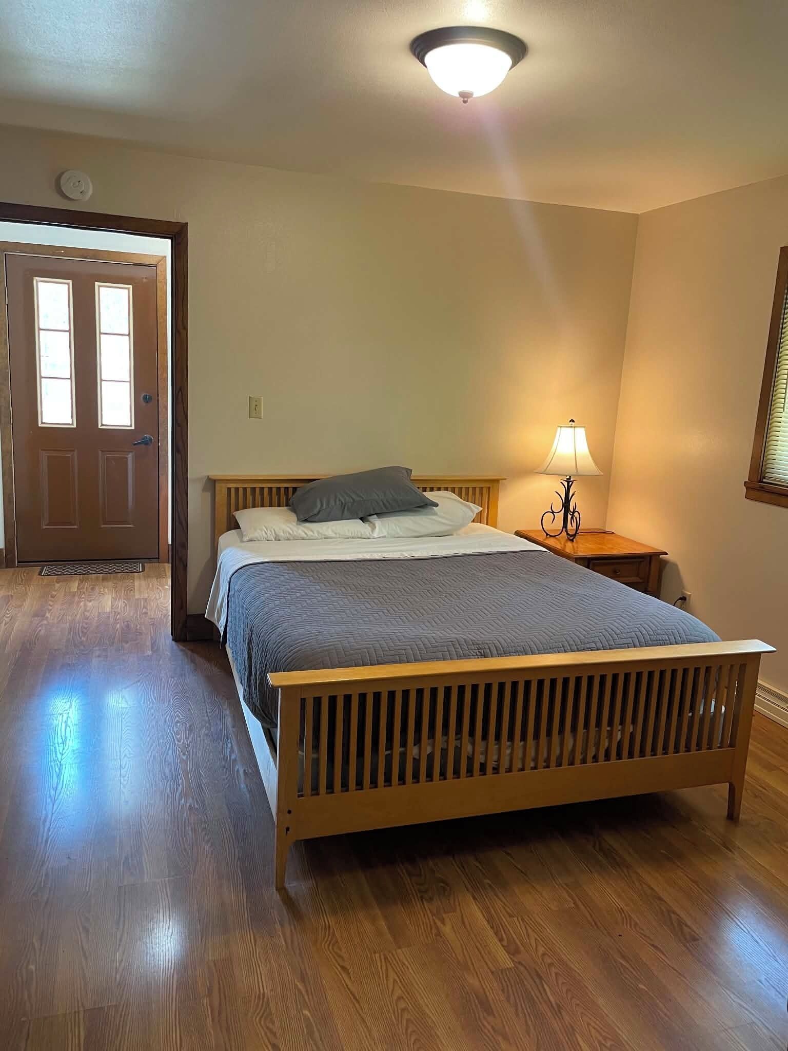 Une chambre à coucher avec un lit en bois, une table de chevet avec une lampe, une porte et une fenêtre.