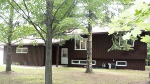 Un bâtiment à deux étages, de couleur brune, avec des bordures blanches autour des fenêtres et des portes. Des arbres se trouvent devant le bâtiment, et une petite antenne parabolique est visible sur le côté.