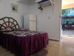 Ein Schlafzimmer mit Bett, einem weißen Kühlschrank, einem Holz-Kopfteil, einer Wand-Klimaanlage und einem kleinen Teppich.