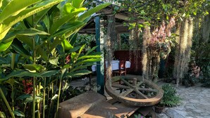 A rustic outdoor area with a large wooden wheel, lush greenery, and a table under a pergola. - Casa Mirian (Candelaria)