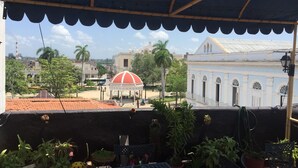 A terrace with a table and chairs, potted plants, and a view of a town with buildings and a dome structure. - Casa Colonial Center (Cienfuegos)