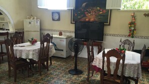 A dining area with wooden chairs and tables, a refrigerator, a clock, and a television on the wall. - Casa Colonial Center (Cienfuegos)