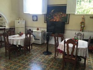 Un coin repas avec des chaises et des tables en bois, un réfrigérateur, une horloge et un téléviseur fixé au mur.