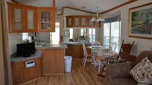A compact kitchen with wooden cabinets, a dining area with white chairs, and a sofa with a patterned cushion. - Camp Mack Lodge, Marina & RV Resort (Lake Wales)