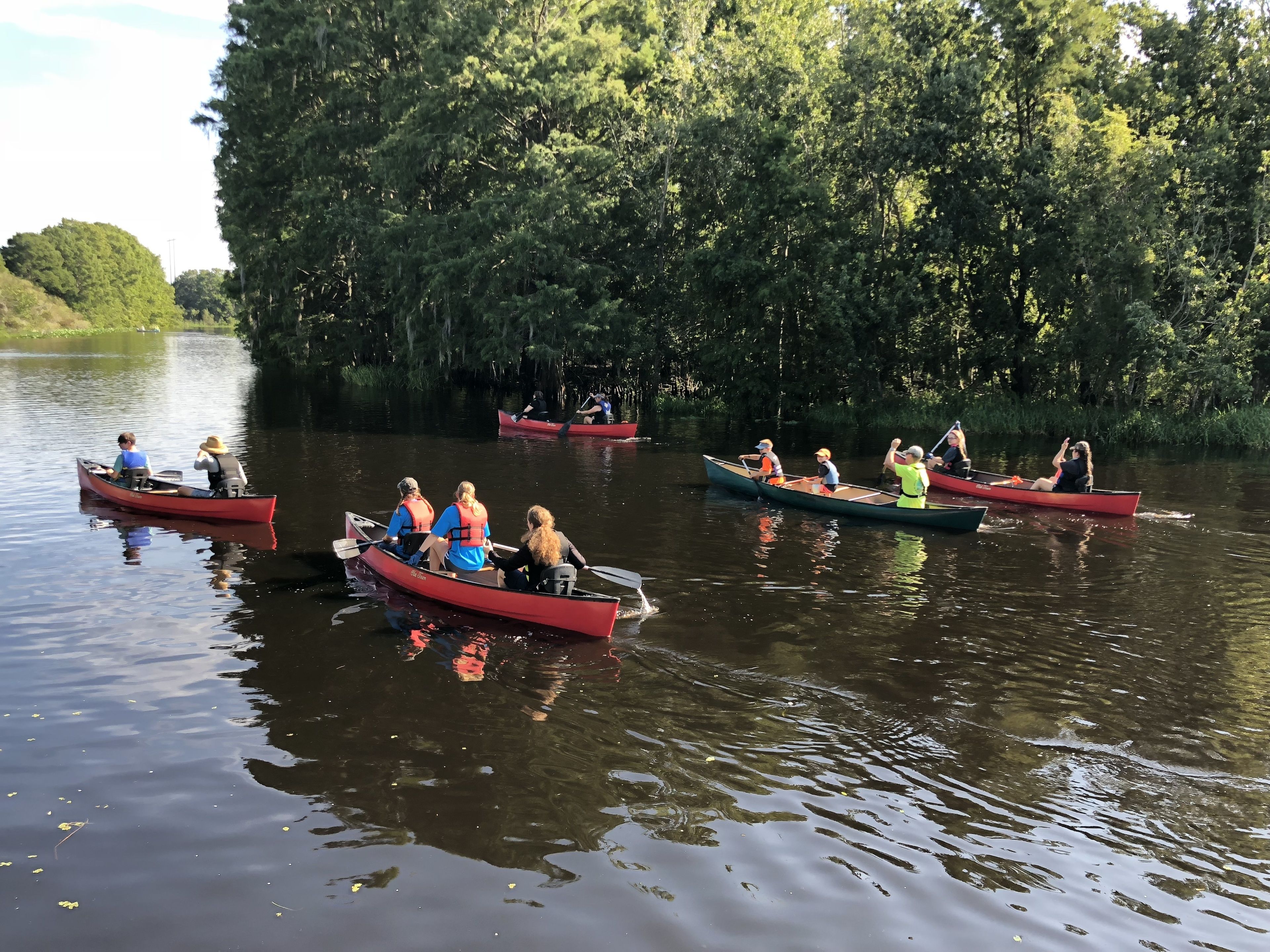 Several canoes on a calm river surrounded by dense trees.