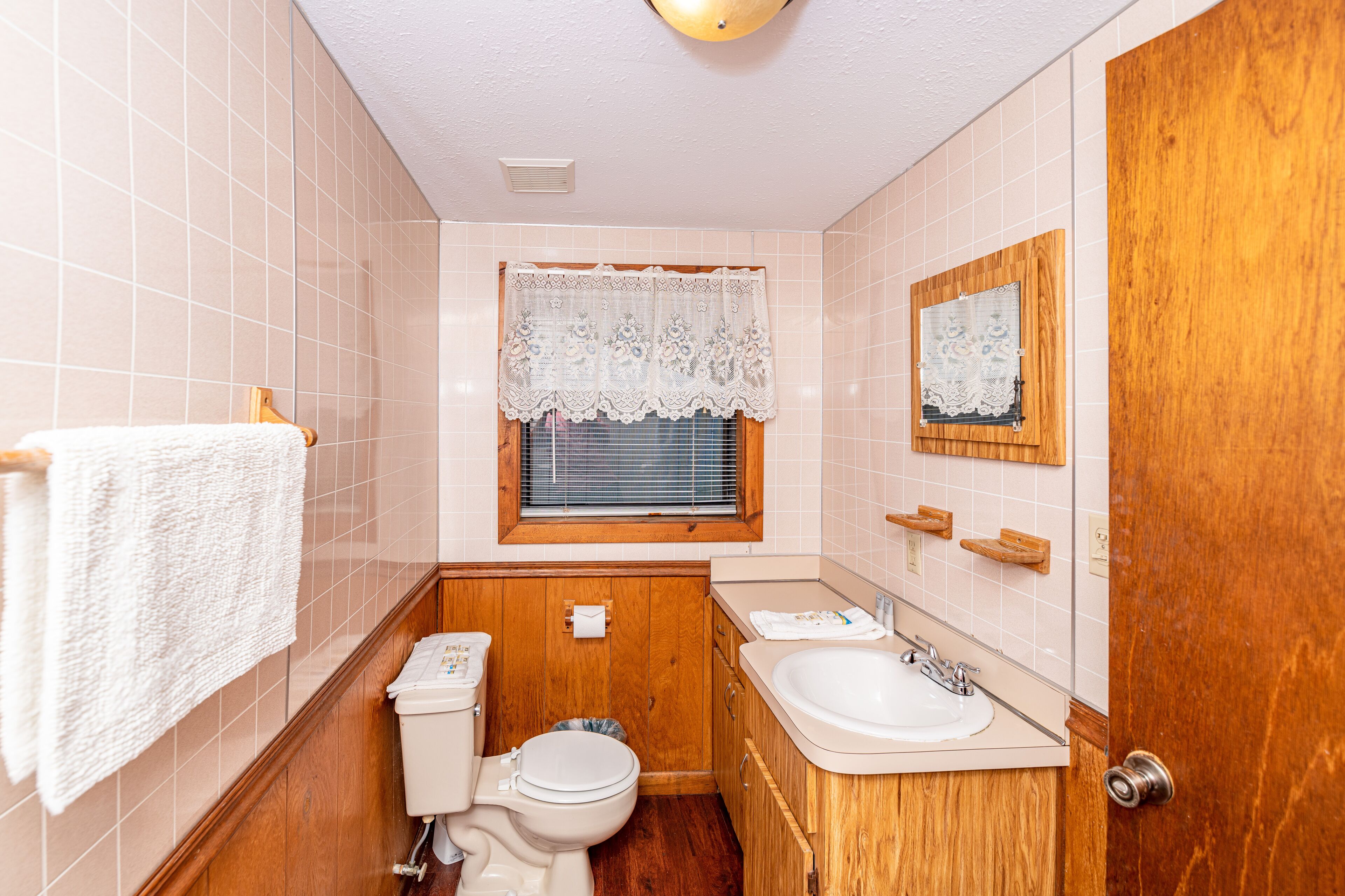 A small bathroom with a toilet, sink, and window with a lace curtain.
