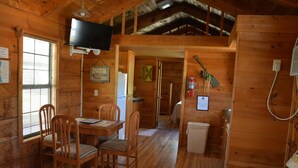 A wooden cabin interior with a dining area, a television mounted on the wall, and a fire extinguisher on the wall. - Camp Mack Lodge, Marina & RV Resort (Lake Wales)