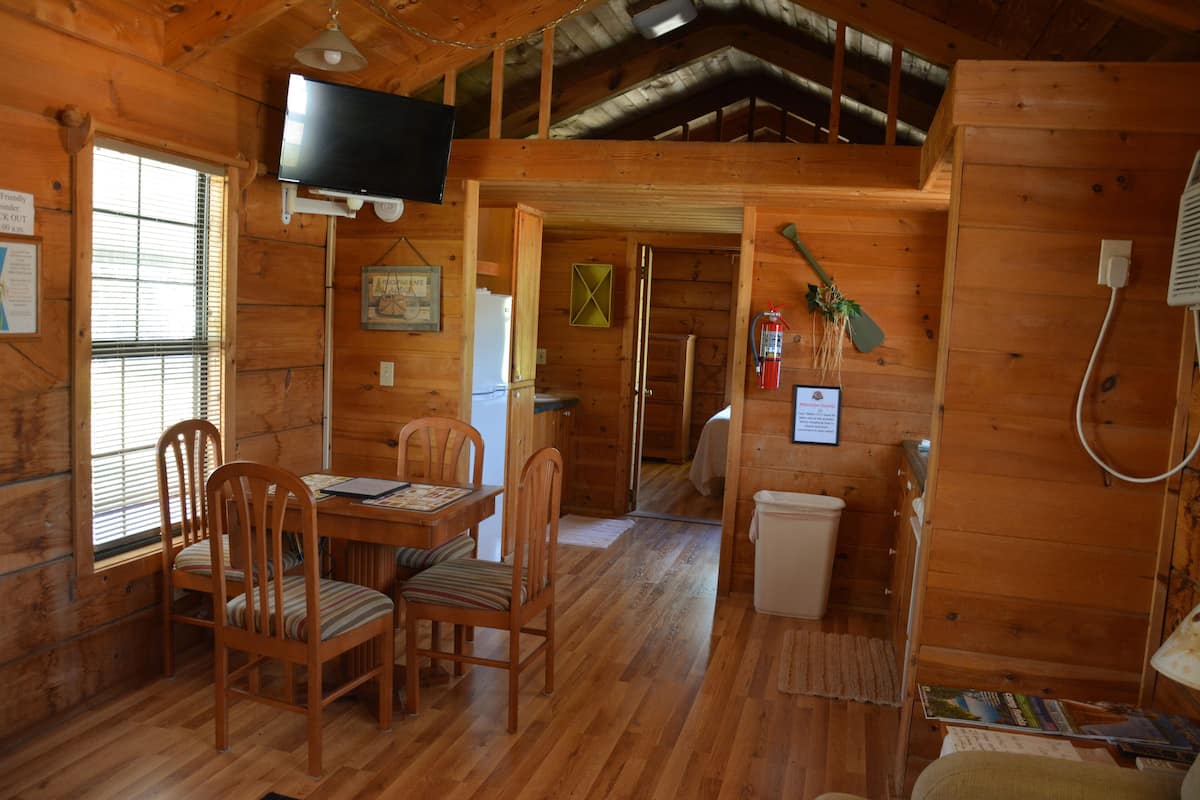 Interior de una cabaña de madera con comedor, televisor montado en la pared y extintor.