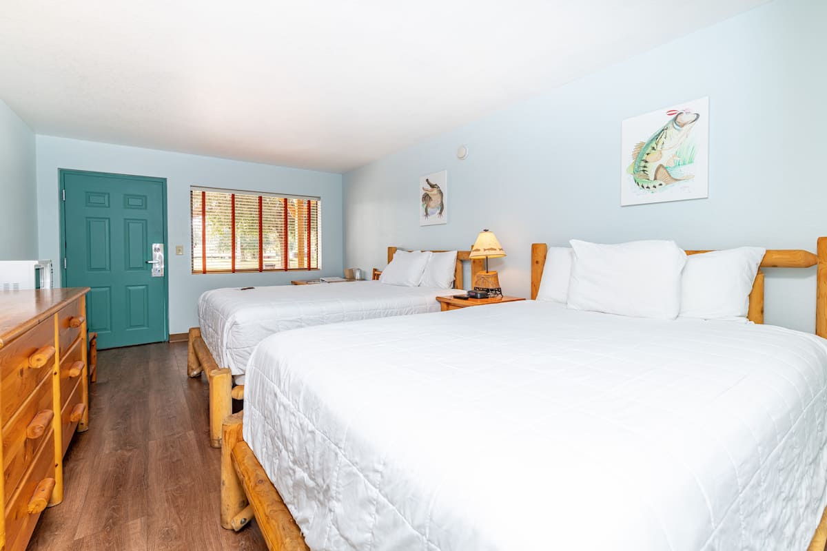 Una habitación con dos camas, un aparador de madera, una puerta verde azulada y una ventana con persianas.