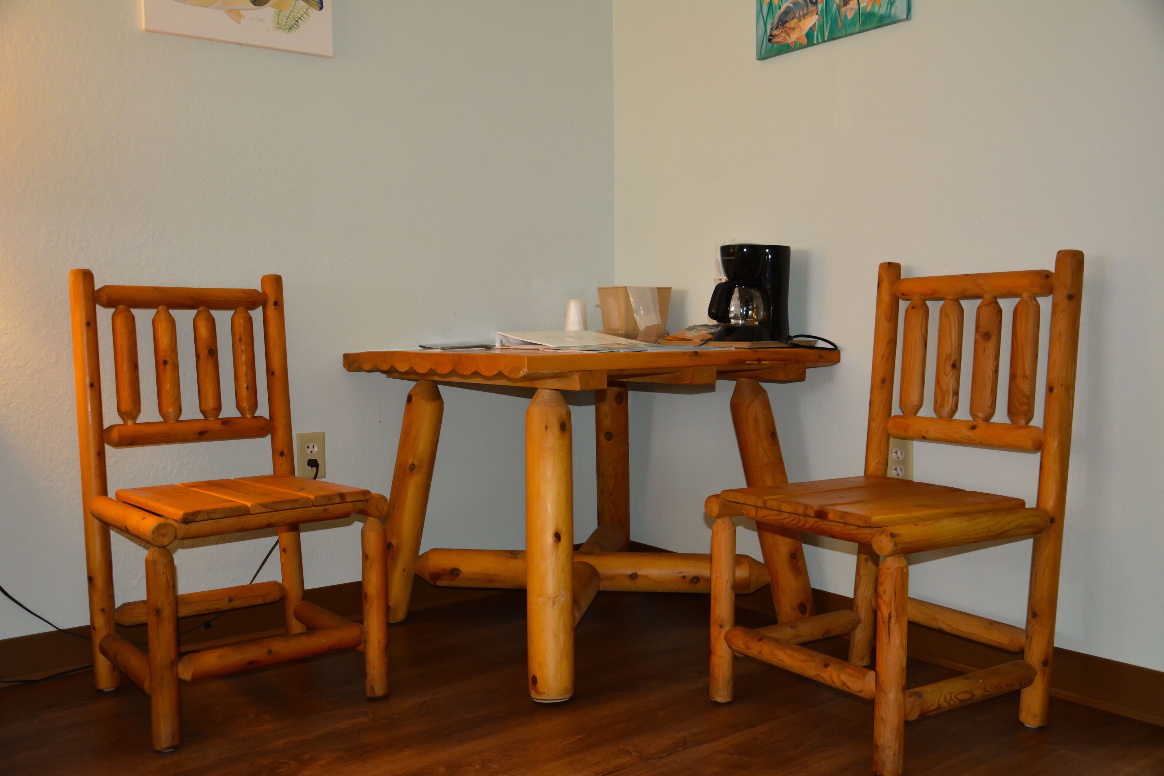 A wooden table with two chairs, a coffee maker, and some papers.