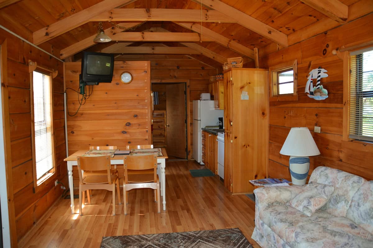 Interior de una cabaña de madera con comedor, cocina y sala de estar con sofá.