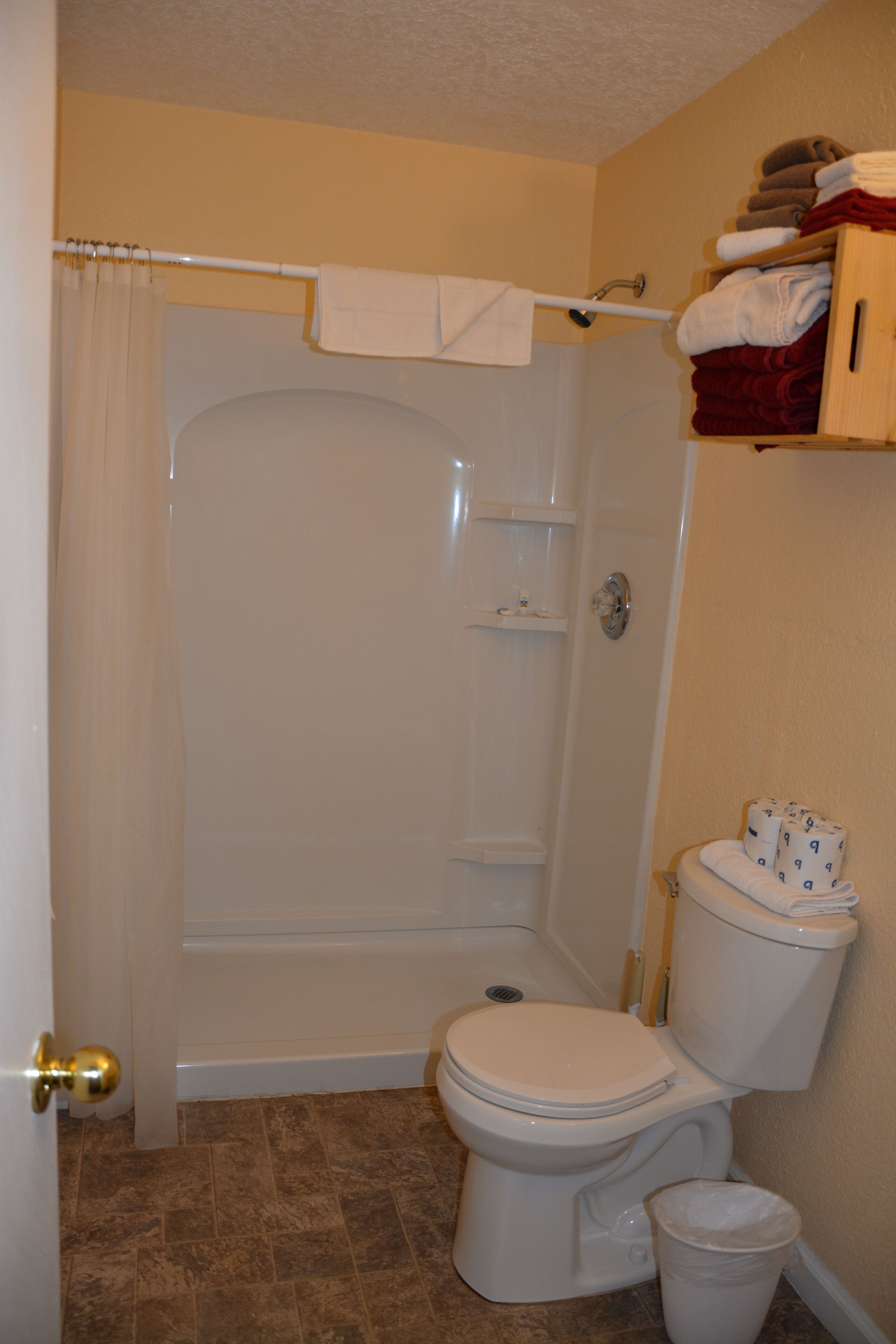 Een badkamer met douche, toilet en een handdoekrek met handdoeken.