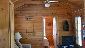 A cozy cabin interior with wooden walls, a ceiling fan, a sofa, a chair, and a rug. - Camp Mack Lodge, Marina & RV Resort (Lake Wales)