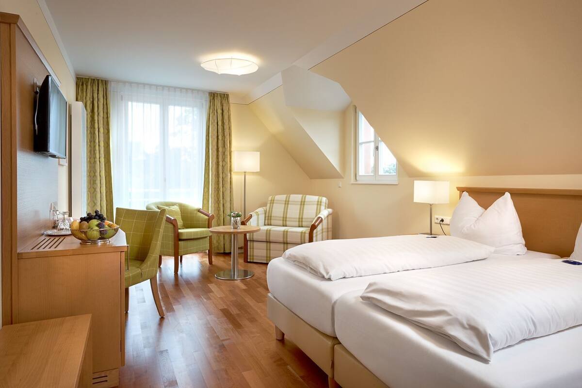 A hotel room with a bed, a desk, a chair, a small table, and a lamp.