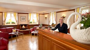 A hotel lobby with a reception desk, red leather sofas, a fireplace, and a large white swan vase. - Flair Hotel Schwanen (Bad Bellingen)