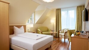 A hotel room with a large bed, two armchairs, a desk with a fruit bowl, a lamp, and a TV. - Flair Hotel Schwanen (Bad Bellingen)