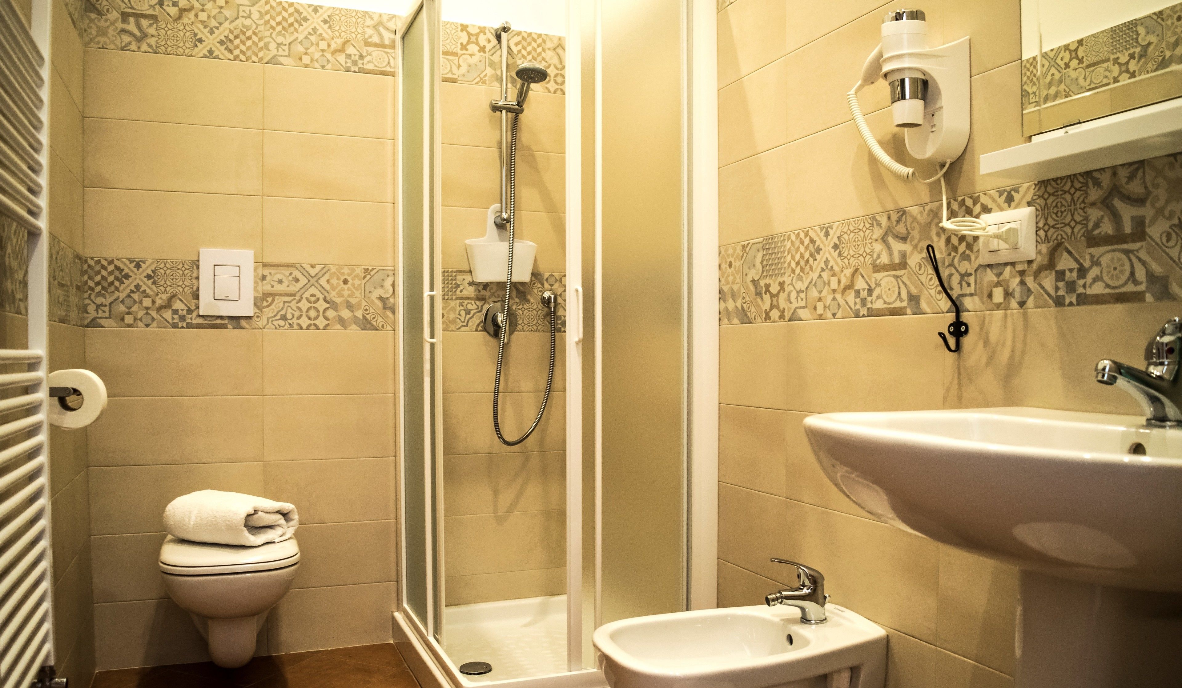 Une salle de bain avec douche, toilettes, lavabo et carrelage à motifs.