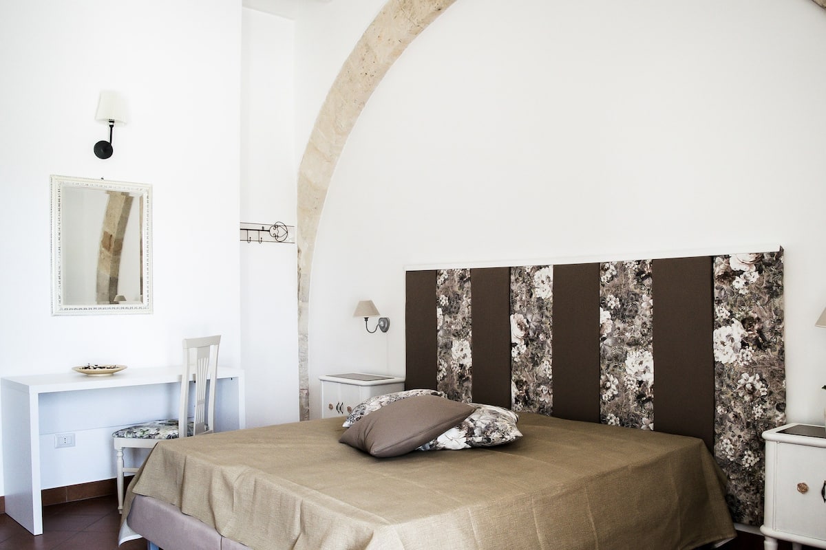 Ein Schlafzimmer mit einem Bett, einem Schreibtisch, einem Stuhl, einem Nachttisch und einer Wandleuchte.