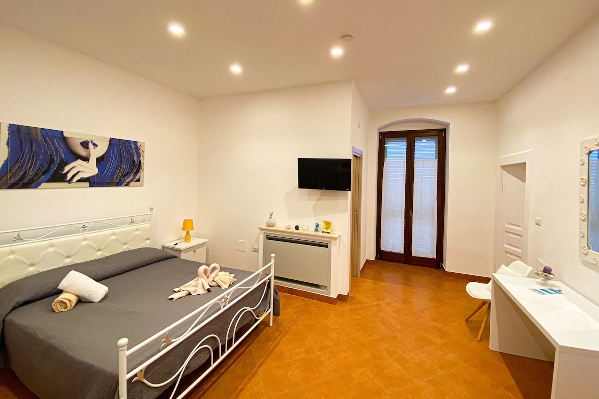 Ein Schlafzimmer mit Bett, Schreibtisch, Fernseher und Tür.