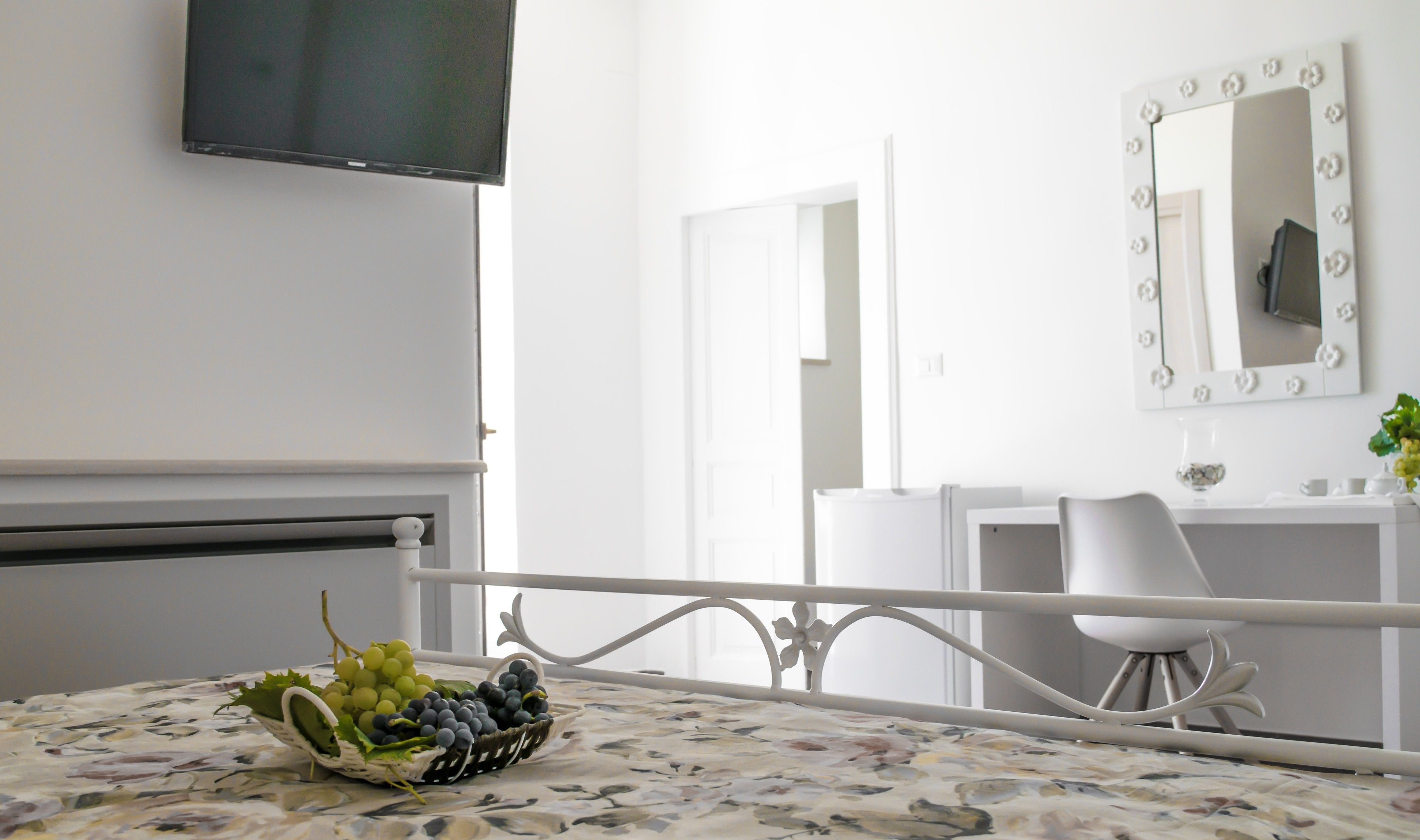 Hotelkamer met een bed, een aan de muur bevestigde televisie, een spiegel met verlichting, een wit bureau en een stoel.