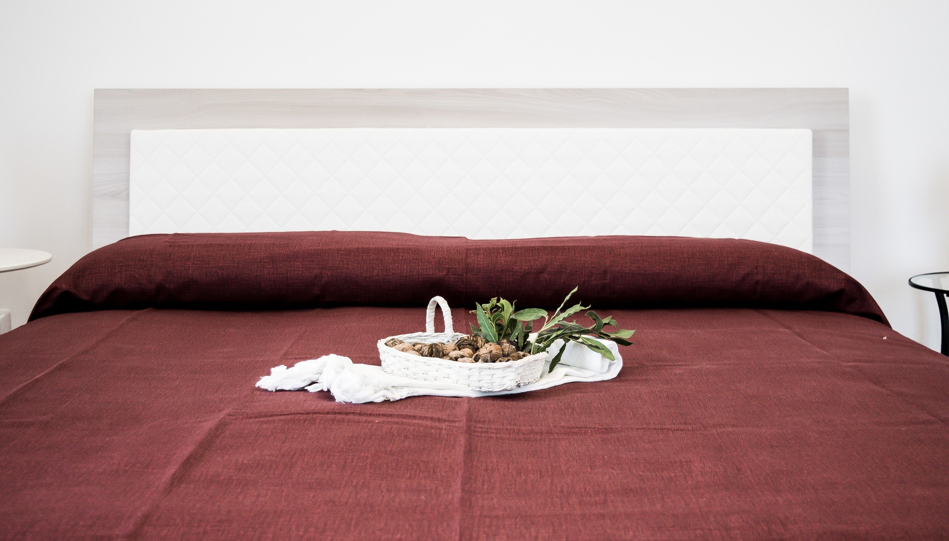 A bed with a red bedspread, a white headboard, and a basket with nuts and a plant on the bed.