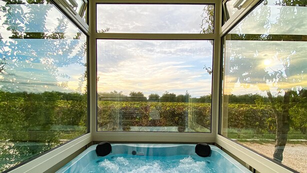 A hot tub with a view of a garden and trees through large windows. - Tenuta Vigna Del Noce (Corato)