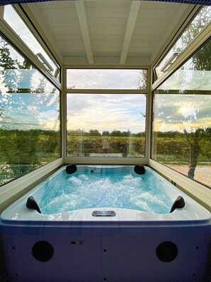 Un jacuzzi con vistas a un jardín y árboles a través de amplios ventanales.