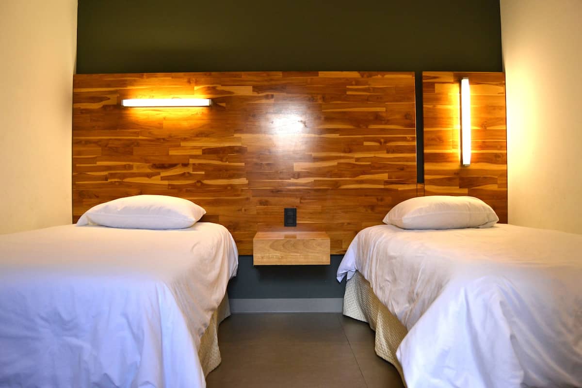 Una camera d'albergo con due letti, una testiera in legno, lampade ai lati del letto e un comodino in legno.